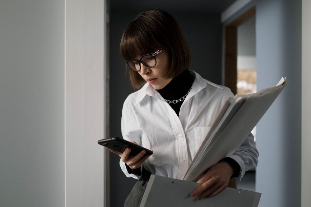 Frau mit Aktenordner und Smartphone im Büro
