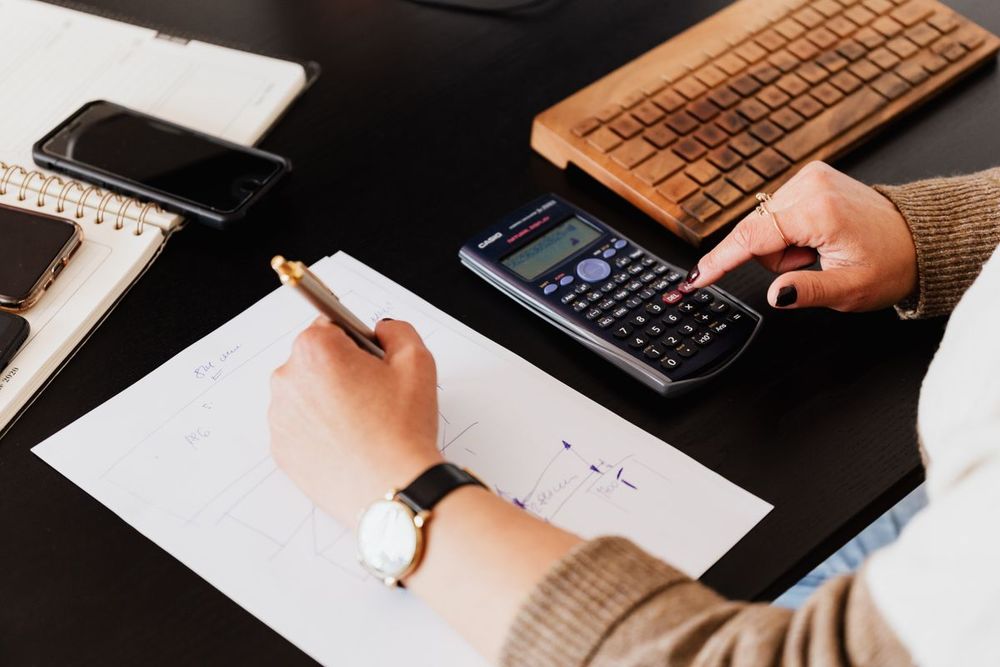 Hand mit Stift und Taschenrechner über Buchhaltungsunterlagen